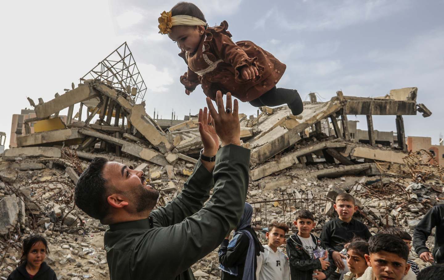 A man tosses a baby into the air as Palestinian children receive Eid treats distributed volunteers of a charity organization on the second day of Eid al-Fitr amid rubbles in Khan Yunis, Gaza, on March 21, 2026.
