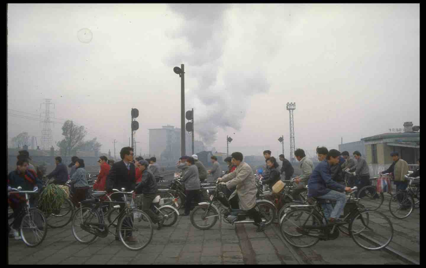 Cyclists waiting at railroad crossing in Shenyang, China, 1990.