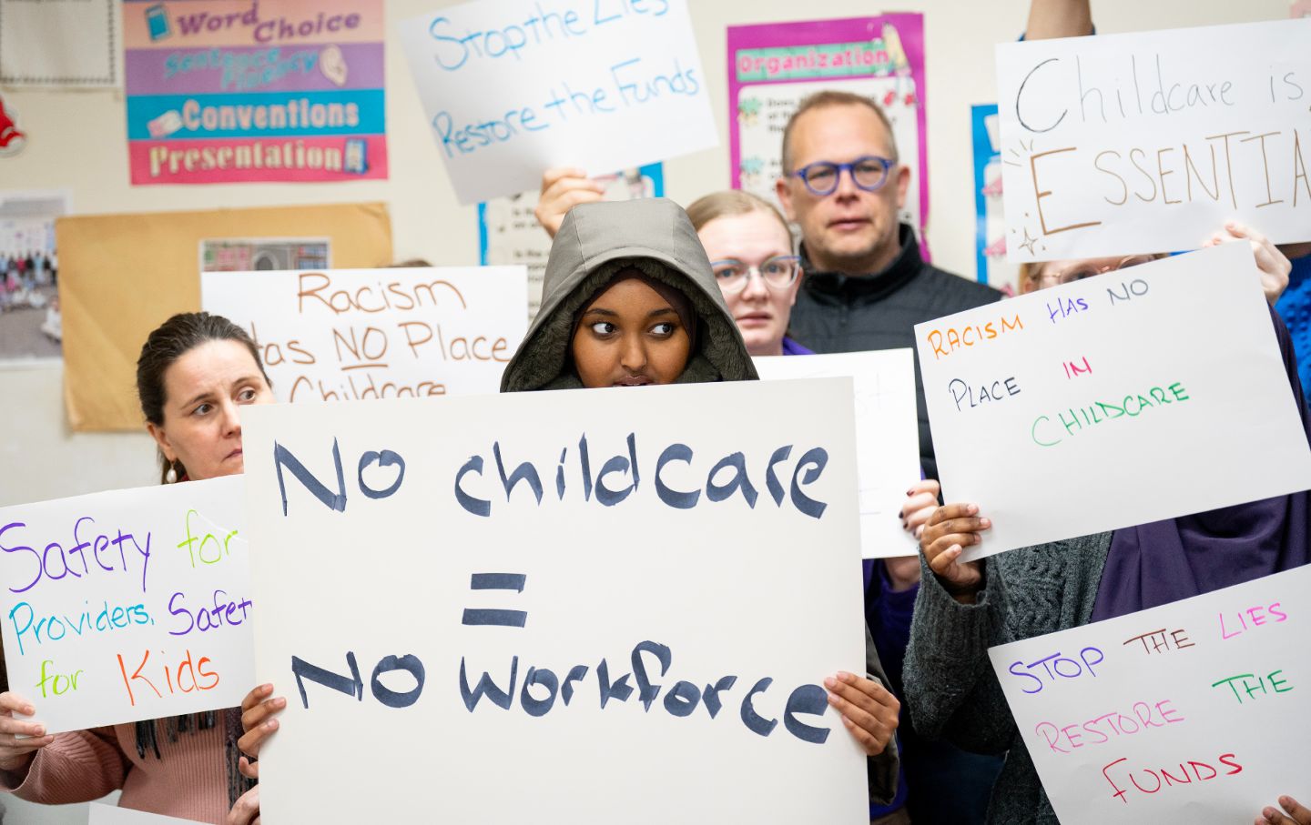 Parents, teachers, childcare workers, and community members hold up handmade signs defending local childcare programs during a press conference at a daycare center in Minneapolis, Minnesota.